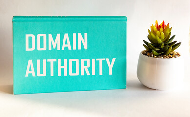 Domain Authority, the text is written on a green notepad and a white background, next to a cactus flower. The concept means a computed metric of the probability of ranking a domain.
