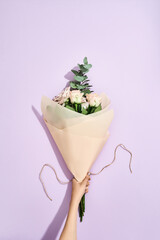 Perfect present for her. Female hands making fresh flowers bouquet on purple background, top view