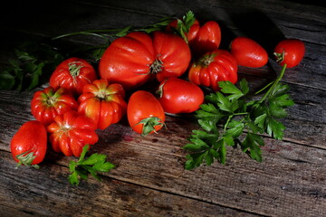 A group of freshly washed tomatoes and parsley is lying on a table of old boards.Dark background. Tomatoes and parsley are ingredients of vegan, Keto and Paleo diets. Detox, cleanse. 
