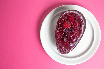 Top view of a red fruits stuffed easter egg on a white plate on a pink background.