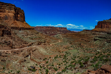 Dirt road at the bottom of the canyon among the layered geological formations of red rocks.