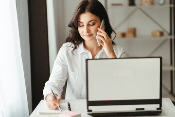 Young business woman multitasking working with laptop and documents and speaking by phone....