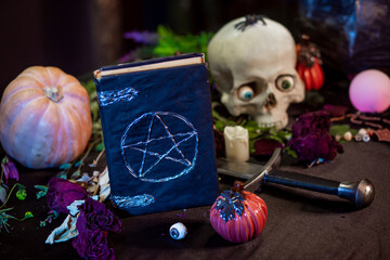 Black book with pentagram, skull and cauldron on the table with witchcraft ingredients. Halloween...