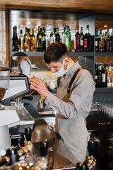 A masked barista prepares delicious coffee at the bar in a cafe. The work of restaurants and cafes during the pandemic.