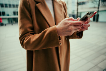 Caucasian business woman typing on cellular device standing in city