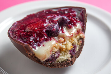 Close up of an opened and cracked red fruits stuffed easter egg on a white plate on a pink background