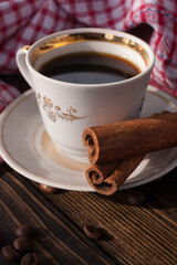A cup of aromatic black coffee and coffee beans on the table with cinnamon sticks. Morning espresso coffee for breakfast in a beautiful white cup.