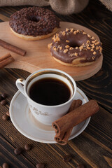 A cup of aromatic black coffee and coffee beans on the table. Morning espresso coffee for breakfast in a beautiful white cup. With a delicious donut in the background. 