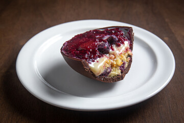 Opened and cracked red fruits stuffed easter egg on a white plate on a wooden table.