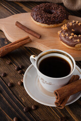 A cup of aromatic black coffee and coffee beans on the table with cinnamon sticks. Morning espresso coffee for breakfast in a beautiful white cup. With a delicious donut in the background.