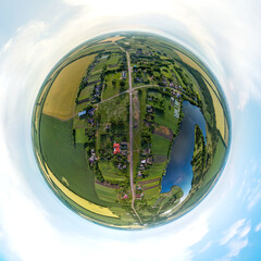 little planet pano - summer landscape over a farm near a blue lake under the sky with storm clouds among green and yellow fields on a summer day