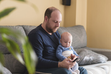 Caucasian father talking on mobile phone to work online with his newborn baby. Single dad taking care of his son. Happy family and work at home