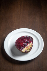 Opened and cracked red fruits stuffed easter egg on a white plate on a wooden table.