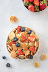 Tiny pancake cereal in a bowl with strawberry and blueberry