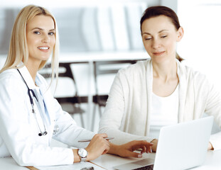 Obraz premium Woman-doctor sitting and communicating with her female patient in clinic. Blonde physician happy to help. Medicine concept