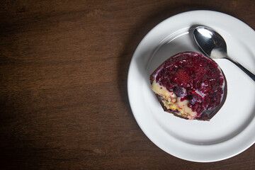 Top view of an opened and cracked red fruits stuffed easter egg on a white plate with a spoon on a wooden table.