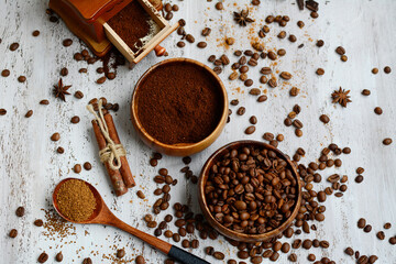 Top view of coffee beans and ground coffee in wooden bowls, coffee grinder, cinnamon sticks on a light aged background.
