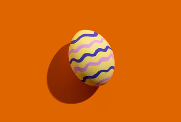 Fototapeta na wymiar Easter egg. Festive decoration. Spring holiday. Gift card. Abstract background. Yellow painted paschal symbol with colorful zigzag lines pattern isolated on orange copy space.