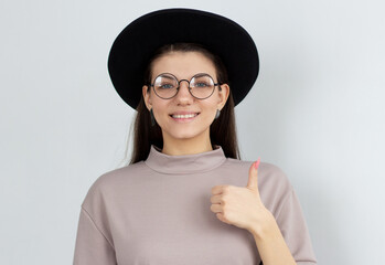 Happy young female wearing beige t-shirt making thumb up sign and smiling cheerfully, showing her support and respect to someone. Body language. I like that. Good job.