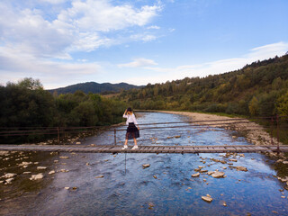 Beautiful woman in hat and dress walk on wooden bridge across mountain river. Aerial top view, travel concept