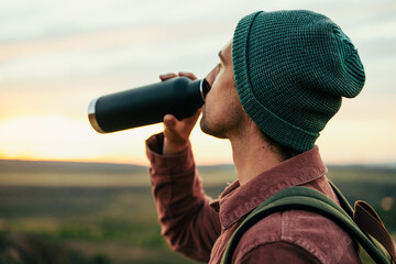 Caucasian male adventurer wearing beanie hiking in mountain quenching thirst drinking water 