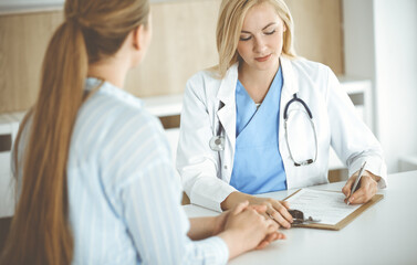 Woman-doctor and patient sitting and talking in hospital or clinic. Blonde therapist is cheerfully smiling. Medicine concept