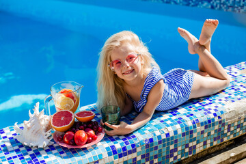 little blonde girl in sunglasses and a striped swimsuit is lying on the side of the pool