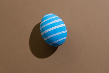Easter egg. Festive decoration. Spring holiday card. Abstract background. Blue painted paschal symbol with white lines pattern isolated on beige copy space.