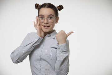 Happy young female teen in stylish modern glasses pointing finger aside at copy space for ad on white studio background
