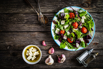 Fresh vegetable salad with feta cheese, tomatoes, arugula, lettuce and roast tomatoes on wooden table
