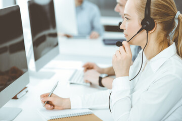 Fototapeta na wymiar Call center. Group of casual dressed operators at work. Blond business woman in headset at customer service office. Telesales in business