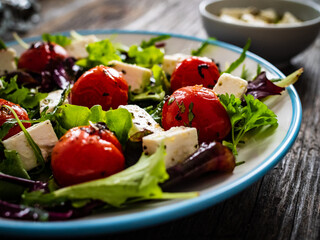 Fresh vegetable salad with feta cheese, tomatoes, arugula, lettuce and roast tomatoes on wooden...