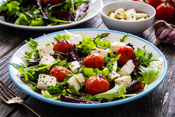 Fresh vegetable salad with feta cheese, tomatoes, arugula, lettuce and roast tomatoes on wooden table
