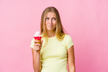 Young russian woman eating an ice cream isolated confused, feels doubtful and unsure.