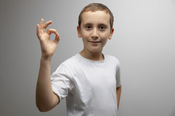 Cute child boy showing okay gesture on gray background with copy space. Agreement, approval, positive feedback concept