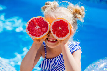 happy little blonde girl in the pool holding a grapefruit. space for text. children's summer...