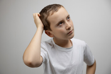 Puzzled caucasian child boy scratch head in confusion thinking on gray studio background, body language concept