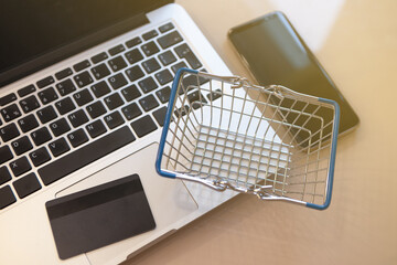 Shopping cart, laptop, mobile phone, credit card on the desktop. Top view, highlights, soft selective focus. Online shopping concept, e-commerce, self-isolation, banking financial transactions