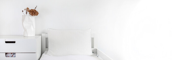 Minimalistic children's room in white colors. A baby bed with white linens , and a dry flower on the table next to it