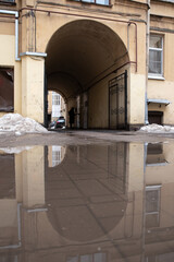 A long city courtyard, with a puddle and an arch in the background