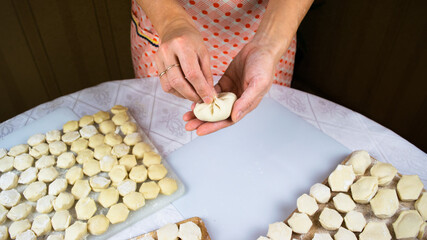 Woman's hands sculpt khinkale dumplings on background of cutting boards with hendmade dumplings, ravioli and khinkali.