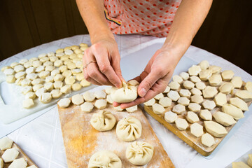 Woman's hands sculpt khinkale dumplings on background of cutting boards with hendmade dumplings, ravioli and khinkali.