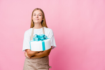 Young russian baker woman holding a delicious cake smiling confident with crossed arms.