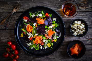 Salmon salad - smoked salmon with feta cheese, avocado and mix of vegetables on wooden table

