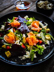 Salmon salad - smoked salmon with feta cheese, avocado and mix of vegetables on wooden table
