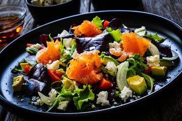 Salmon salad - smoked salmon with feta cheese, avocado and mix of vegetables on wooden table
