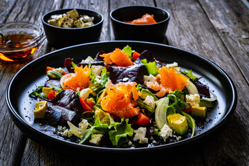 Salmon salad - smoked salmon with feta cheese, avocado and mix of vegetables on wooden table

