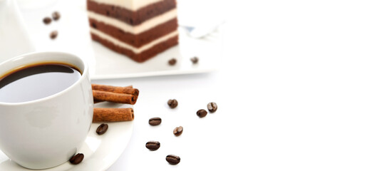 White cup of coffee with cinnamon sticks, cocoa sponge cake on a saucer and scattered coffee beans in close-up. Image with copy space for your advertisement text.
