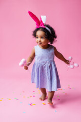 portrait of a cute little girl with Easter bunny ears on her head holding Easter eggs. studio, pink background