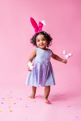 portrait of a cute little girl with Easter bunny ears on her head holding Easter eggs. studio, pink background